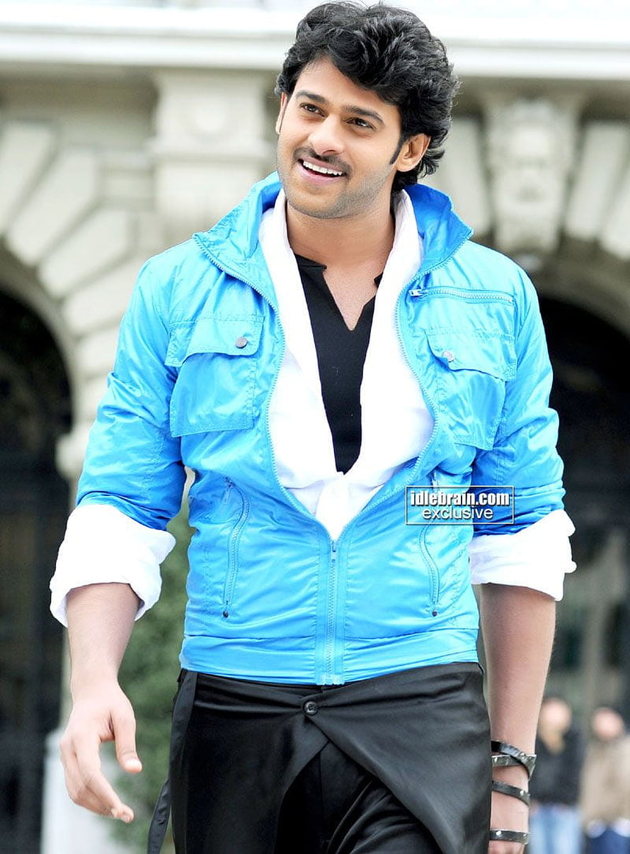 Prabhas in a bright blue jacket and black trousers, smiling outdoors in front of a stone archway HD phone wallpaper