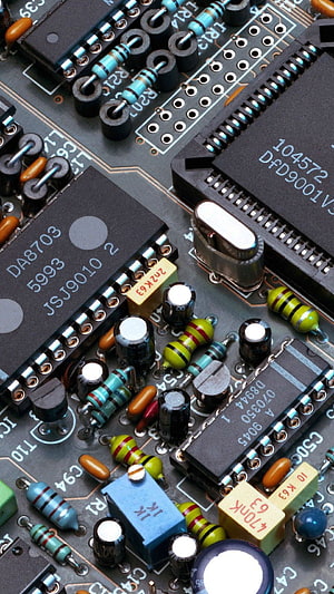 Close-up of a densely populated printed circuit board with integrated circuits, capacitors, and resistors HD phone wallpaper
