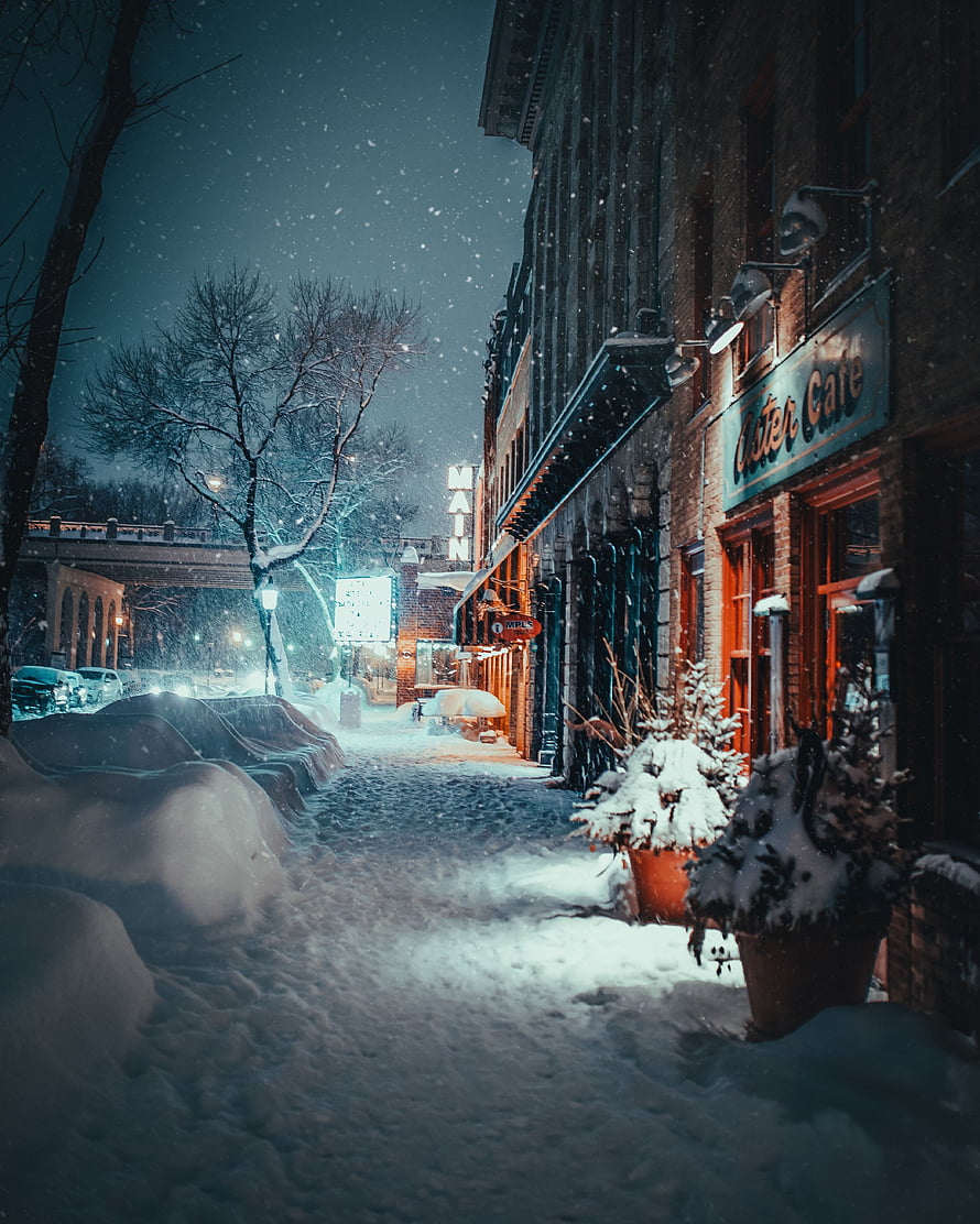 Snowy City Street at Night with Falling Snow and Illuminated Storefronts HD phone wallpaper