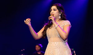Shreya Ghoshal performing live on stage in an elegant white embroidered gown under blue and purple lighting HD wallpaper