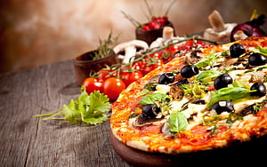 Rustic wood-fired pizza topped with fresh basil, black olives, and mushrooms on a wooden table HD wallpaper