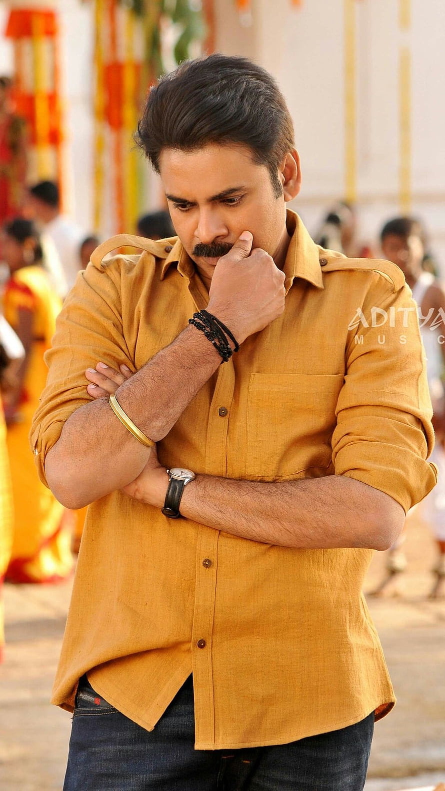 Pawan Kalyan in a mustard shirt with a contemplative expression at a festive event HD phone wallpaper