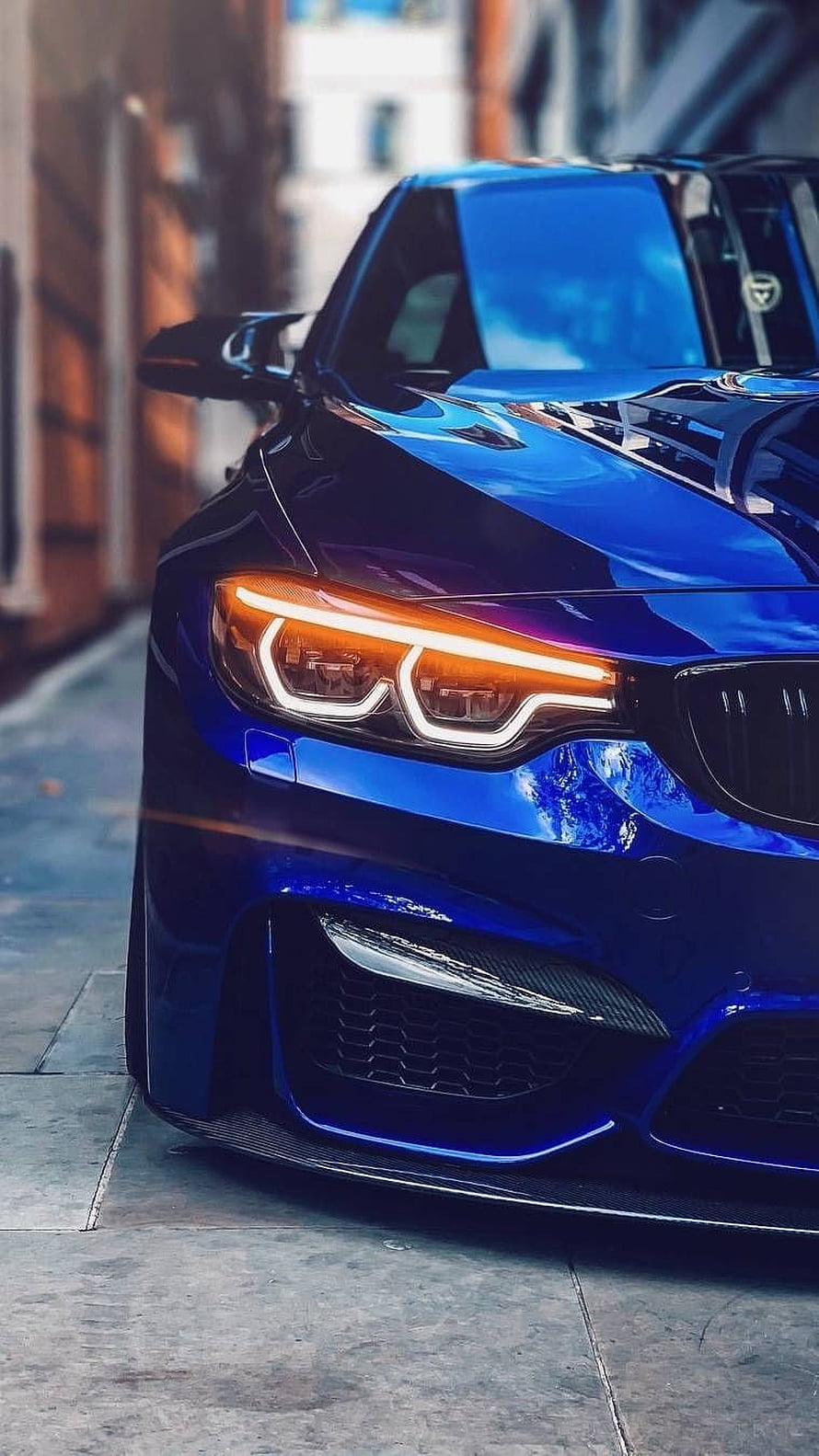 Close-up of a glossy blue BMW M3 front end with illuminated headlights and carbon fiber details HD phone wallpaper