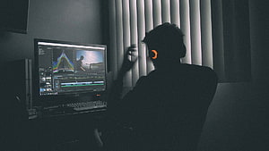 Silhouette of a video editor working late at night in a dimly lit studio with glowing headphones HD wallpaper