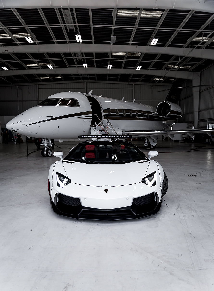 White Lamborghini Aventador parked in front of a private jet inside a hangar HD phone wallpaper