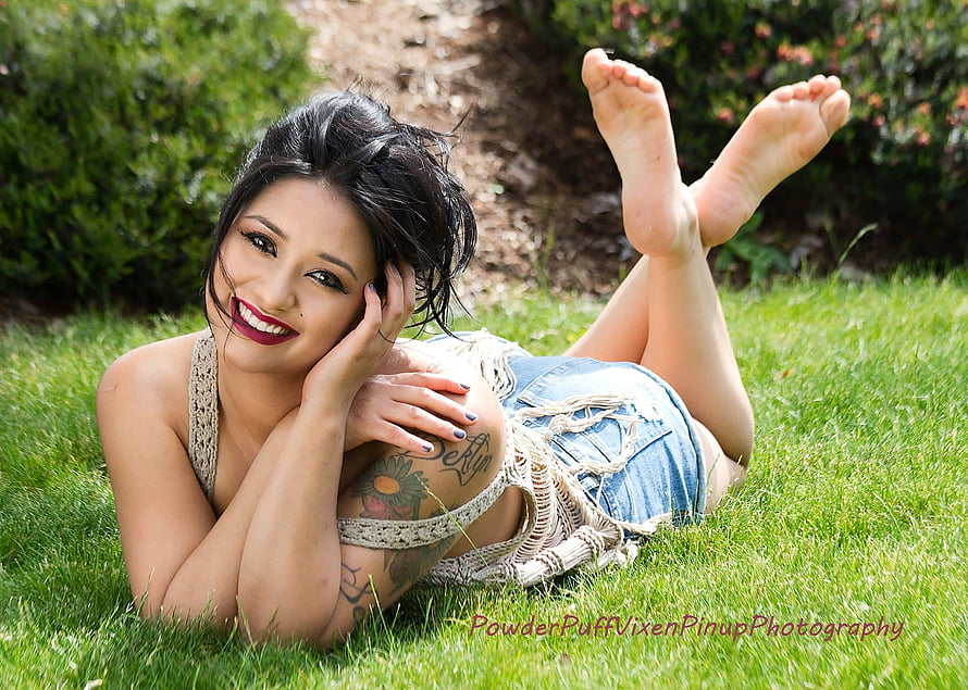 Young woman with tattoos lying on green grass in denim shorts and crochet top HD wallpaper