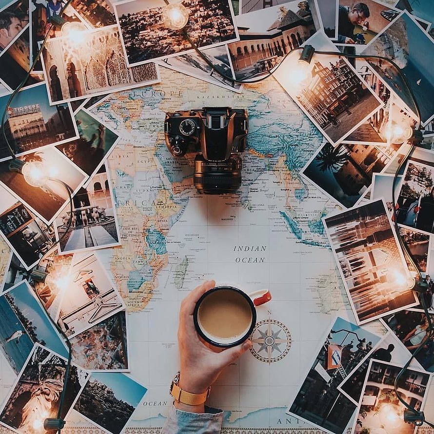 Travel planning flat lay with vintage camera, world map, coffee mug, and scattered travel photos HD phone wallpaper