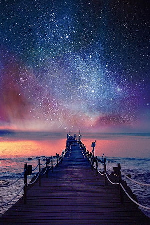 Starry Night Sky Over a Wooden Pier Extending Into a Calm Ocean at Dusk HD phone wallpaper