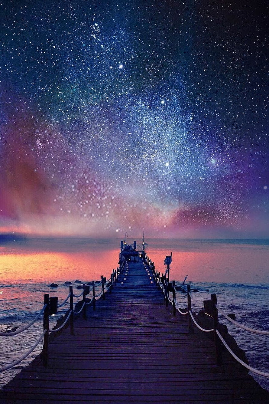 Starry Night Sky Over a Wooden Pier Extending Into a Calm Ocean at Dusk HD phone wallpaper