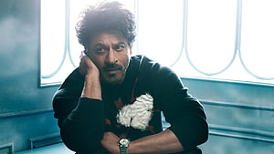 Shah Rukh Khan in a moody portrait with a small white dog against a cool blue interior backdrop HD wallpaper