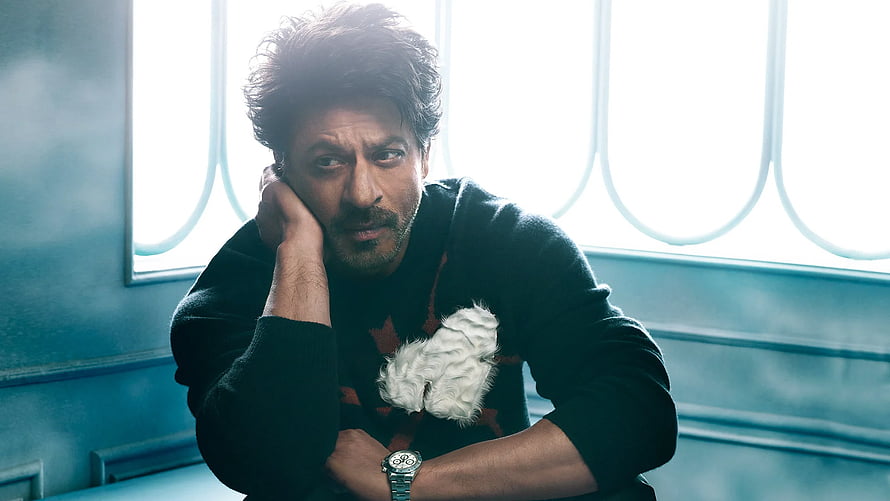 Shah Rukh Khan in a moody portrait with a small white dog against a cool blue interior backdrop HD wallpaper
