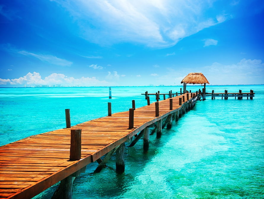 Wooden pier extending into turquoise tropical waters with thatched shelter under a bright blue sky HD wallpaper