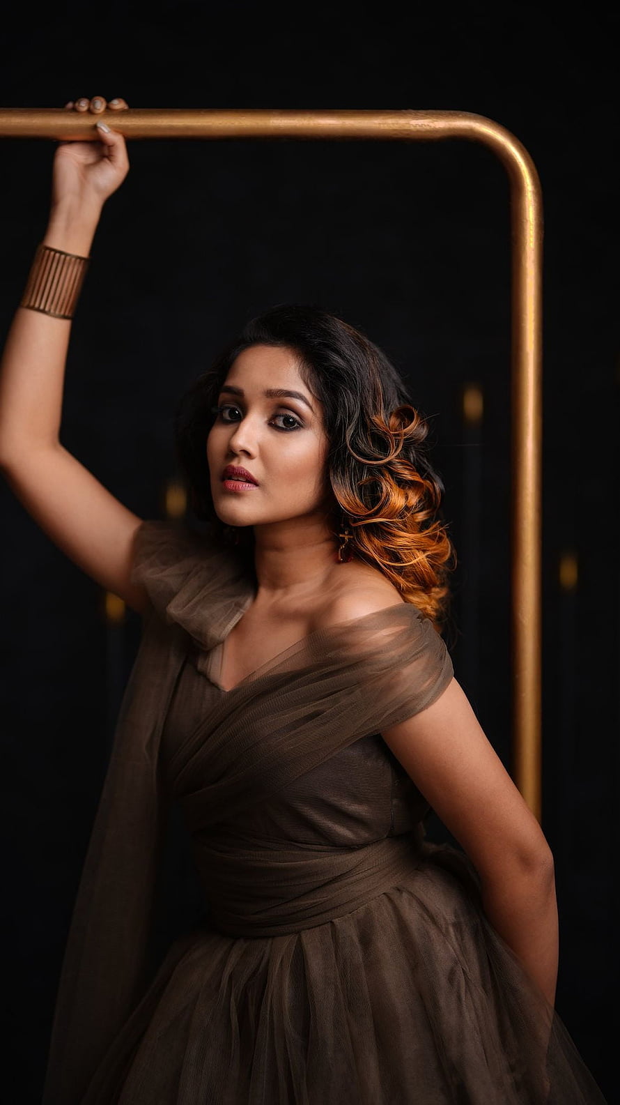 Anikha Surendran in a brown tulle gown posing against a dark backdrop with a gold frame HD phone wallpaper