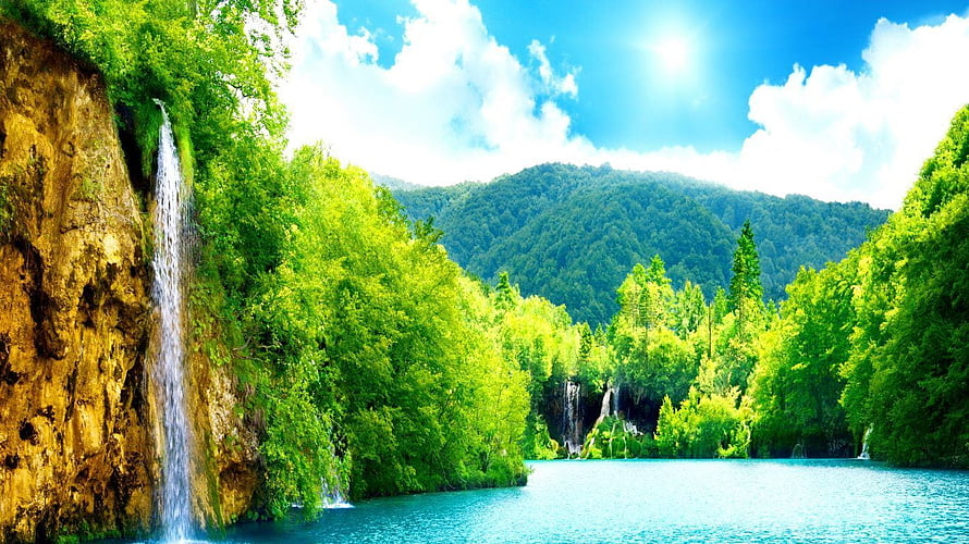 Lush Green Waterfall Cascading Into Turquoise Lake With Forested Hills Under Bright Blue Sky HD wallpaper