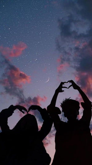 Silhouetted couple forming heart shapes against a starry twilight sky with a crescent moon HD phone wallpaper