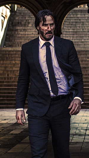 John Wick in a dark suit with a bloodied face standing in a stone archway HD phone wallpaper