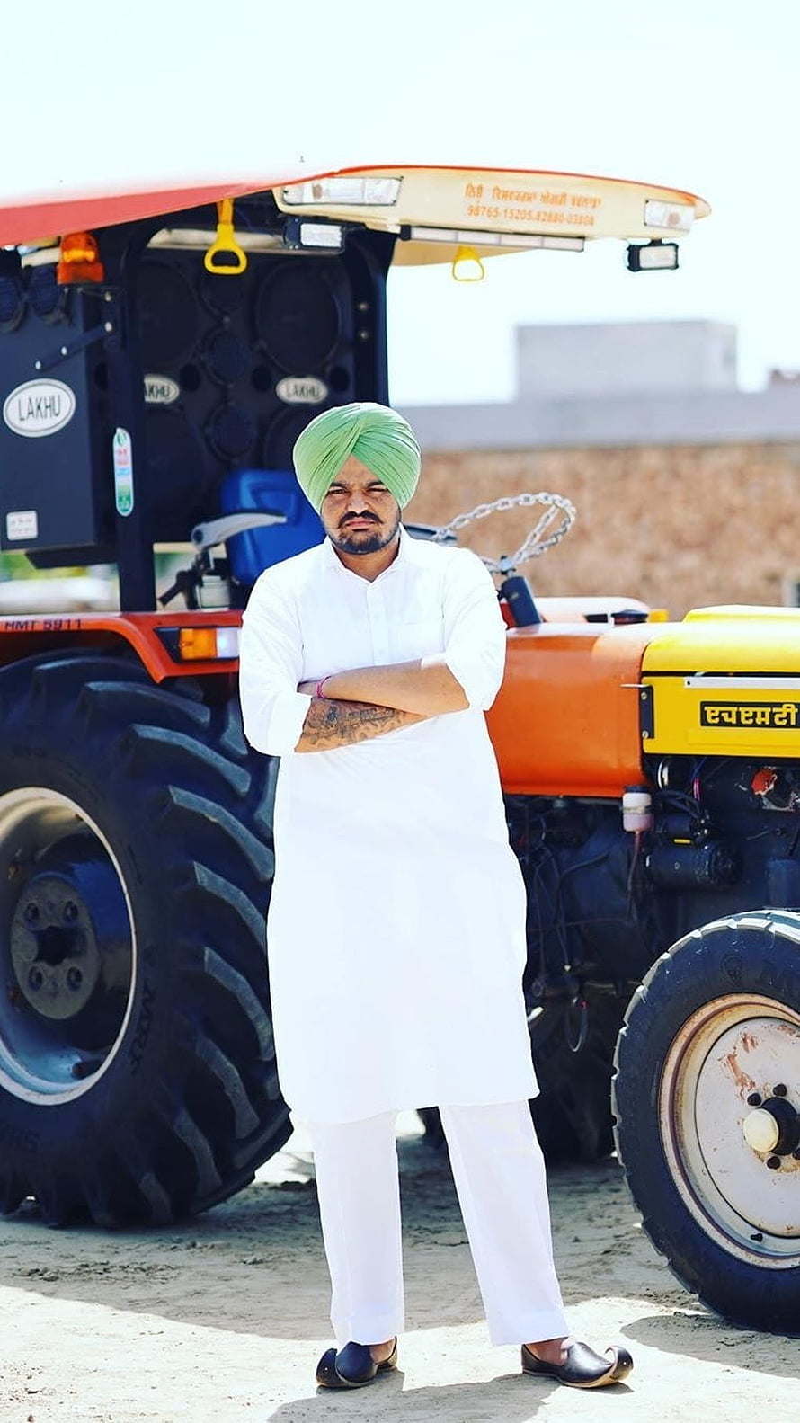 Sidhu Moose Wala in white kurta and green turban standing before a large orange tractor HD phone wallpaper
