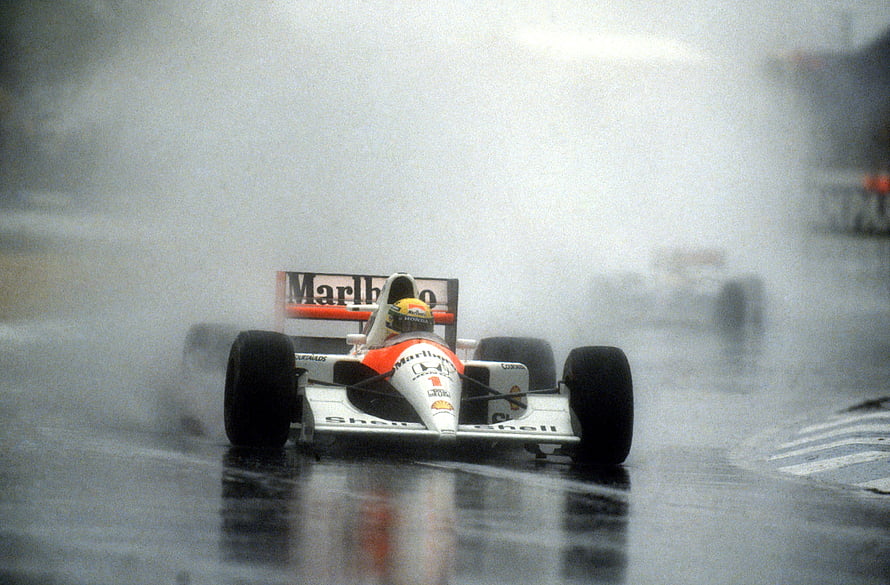Ayrton Senna in a McLaren Formula 1 car racing through heavy rain spray on a wet track HD wallpaper