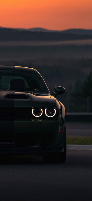 Black Dodge Challenger Front View at Sunset with Glowing Headlights on a Desert Road HD phone wallpaper