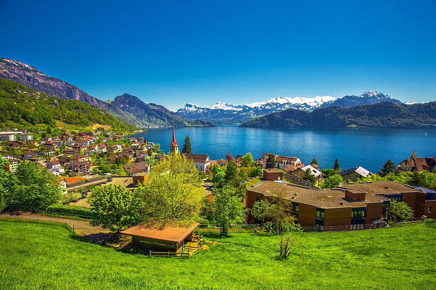 Swiss Alpine Village Overlooking a Deep Blue Lake with Snow-Capped Mountains in Summer HD wallpaper