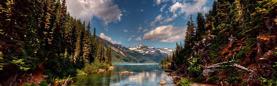 Serene Alpine Lake Framed by Dense Evergreen Forest and Snow-Capped Mountains HD wallpaper