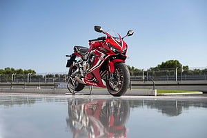 Red Honda CBR650R sport motorcycle parked on a wet racetrack surface with clear blue sky HD wallpaper