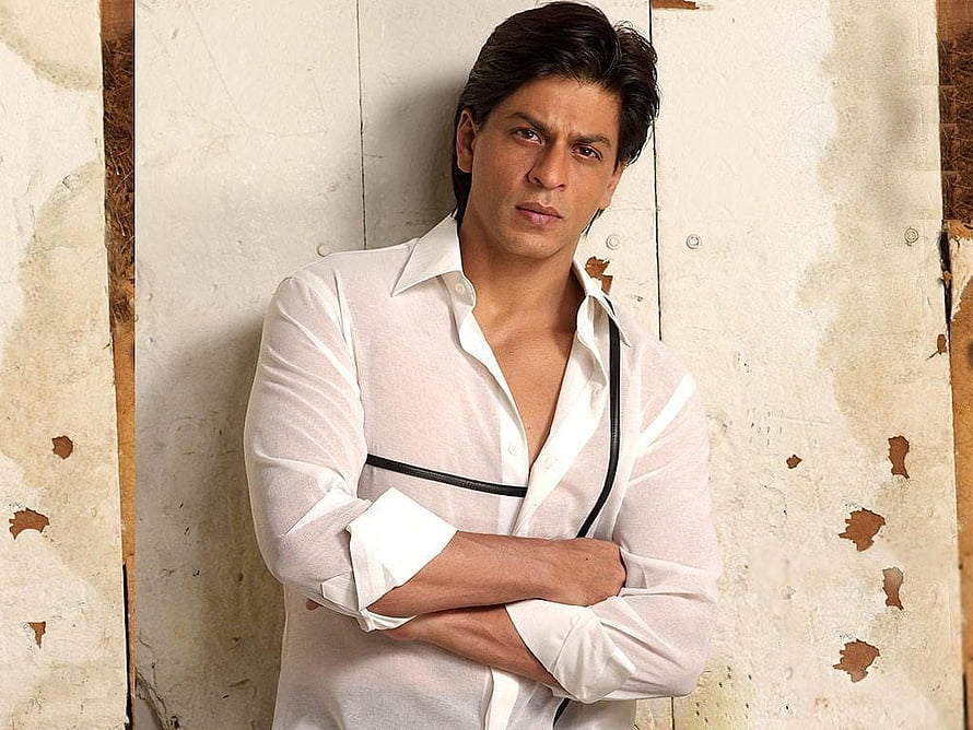 Shah Rukh Khan in a white shirt leaning against a distressed wall with arms crossed HD wallpaper