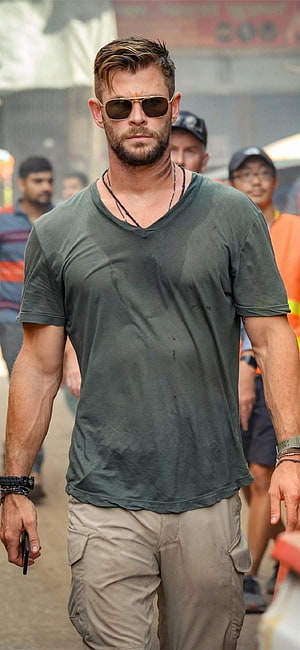 Chris Hemsworth in Extraction wearing a green t-shirt and aviator sunglasses on a busy street HD phone wallpaper