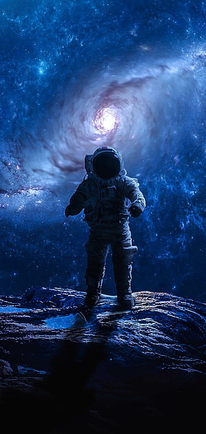 Astronaut Standing on Rocky Terrain Facing a Luminous Cosmic Vortex in Deep Space HD phone wallpaper