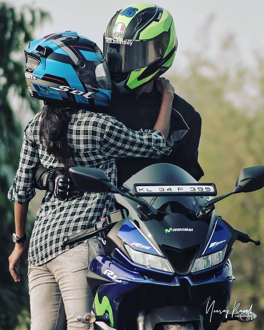Biker couple embracing on a blue Suzuki R15 motorcycle with full-face helmets HD phone wallpaper