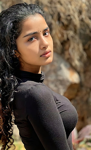Anupama Parameswaran in a black turtleneck with long curly hair against a rocky background HD phone wallpaper