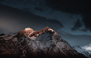 Dramatic Snow-Capped Mountain Peak Under Dark Stormy Sky at Dusk HD wallpaper
