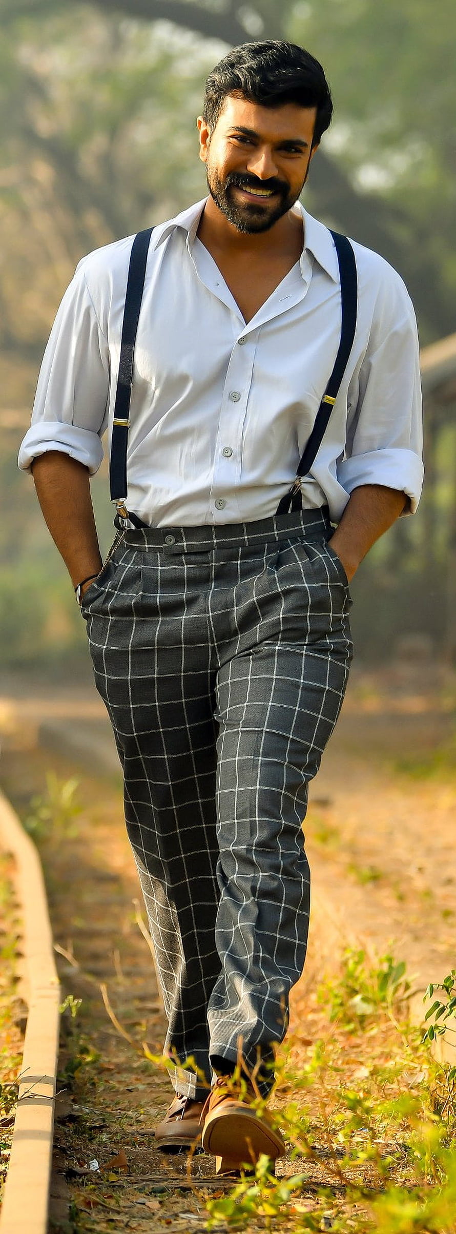 Ram Charan in White Shirt and Checkered Trousers Walking on a Sunlit Path HD phone wallpaper