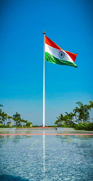Indian National Flag Flying High Over a Reflective Water Pool Under a Clear Blue Sky HD phone wallpaper