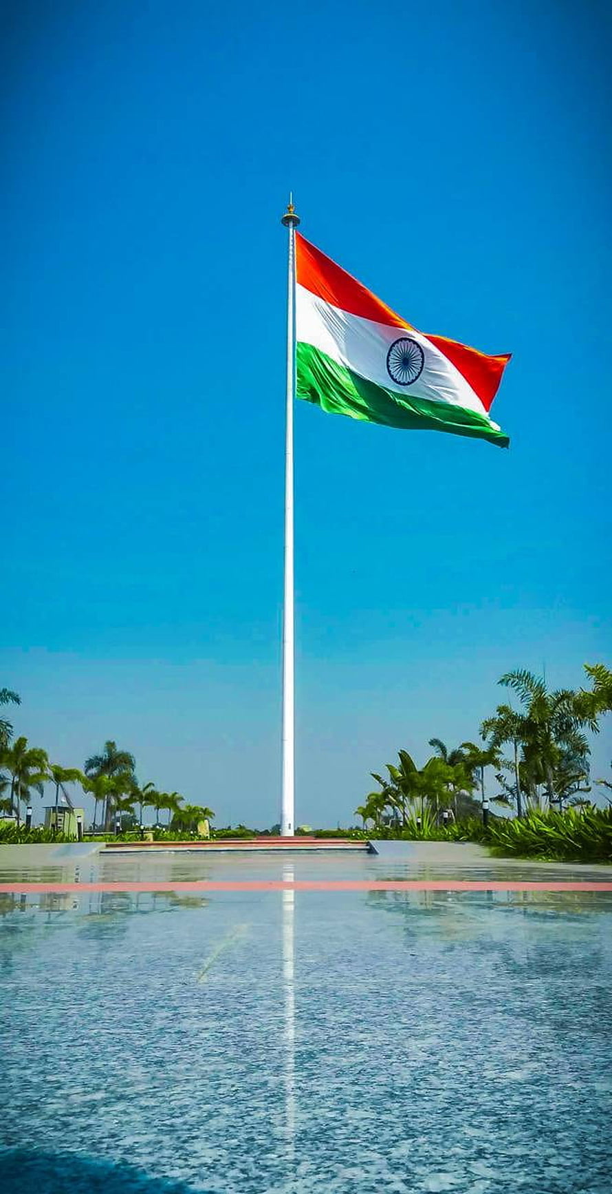 Indian National Flag Flying High Over a Reflective Water Pool Under a Clear Blue Sky HD phone wallpaper