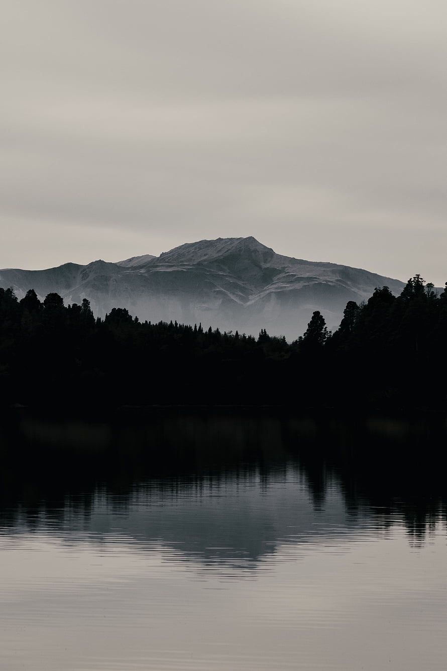 Moody Mountain Lake Reflection with Dark Forest Silhouette Under Overcast Sky HD phone wallpaper