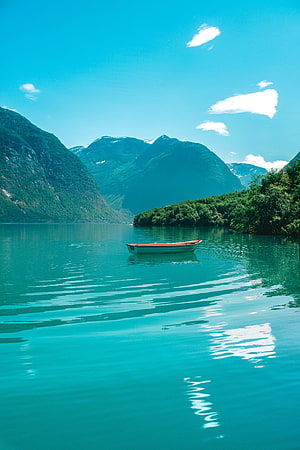 Serene turquoise lake with a small wooden boat floating near lush green mountains under a bright blue sky HD phone wallpaper