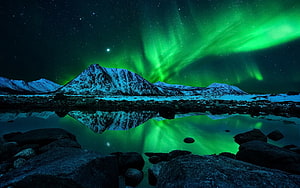 Vibrant green aurora borealis dancing over snow-capped mountains reflected in a calm alpine lake at night HD wallpaper