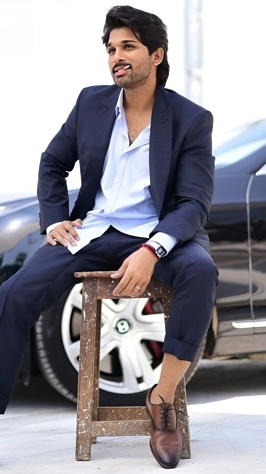 Allu Arjun in a navy suit and light blue shirt sitting on a wooden stool in front of a car HD phone wallpaper