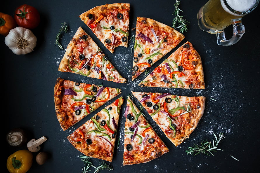 Sliced vegetable pizza with beer and fresh ingredients on a dark slate surface HD wallpaper
