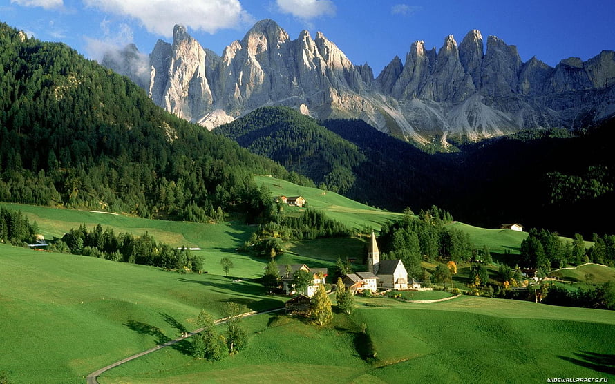 Alpine Village with Church and Farmhouses in Green Pastures Beneath Dramatic Dolomite Peaks HD wallpaper