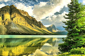 Serene Mountain Lake Reflection with Golden Slopes and Evergreen Trees Under Dramatic Skies HD wallpaper
