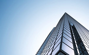 Low-angle view of a modern glass skyscraper rising against a clear blue sky HD wallpaper