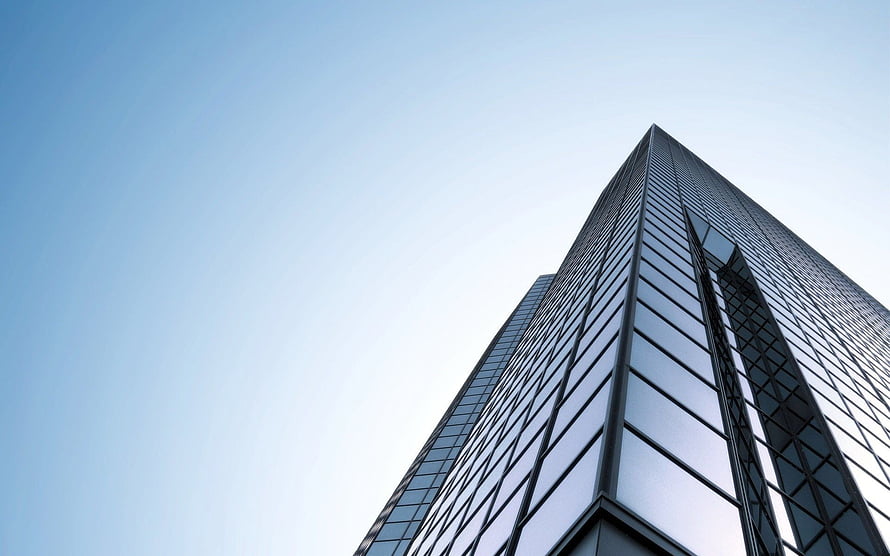 Low-angle view of a modern glass skyscraper rising against a clear blue sky HD wallpaper