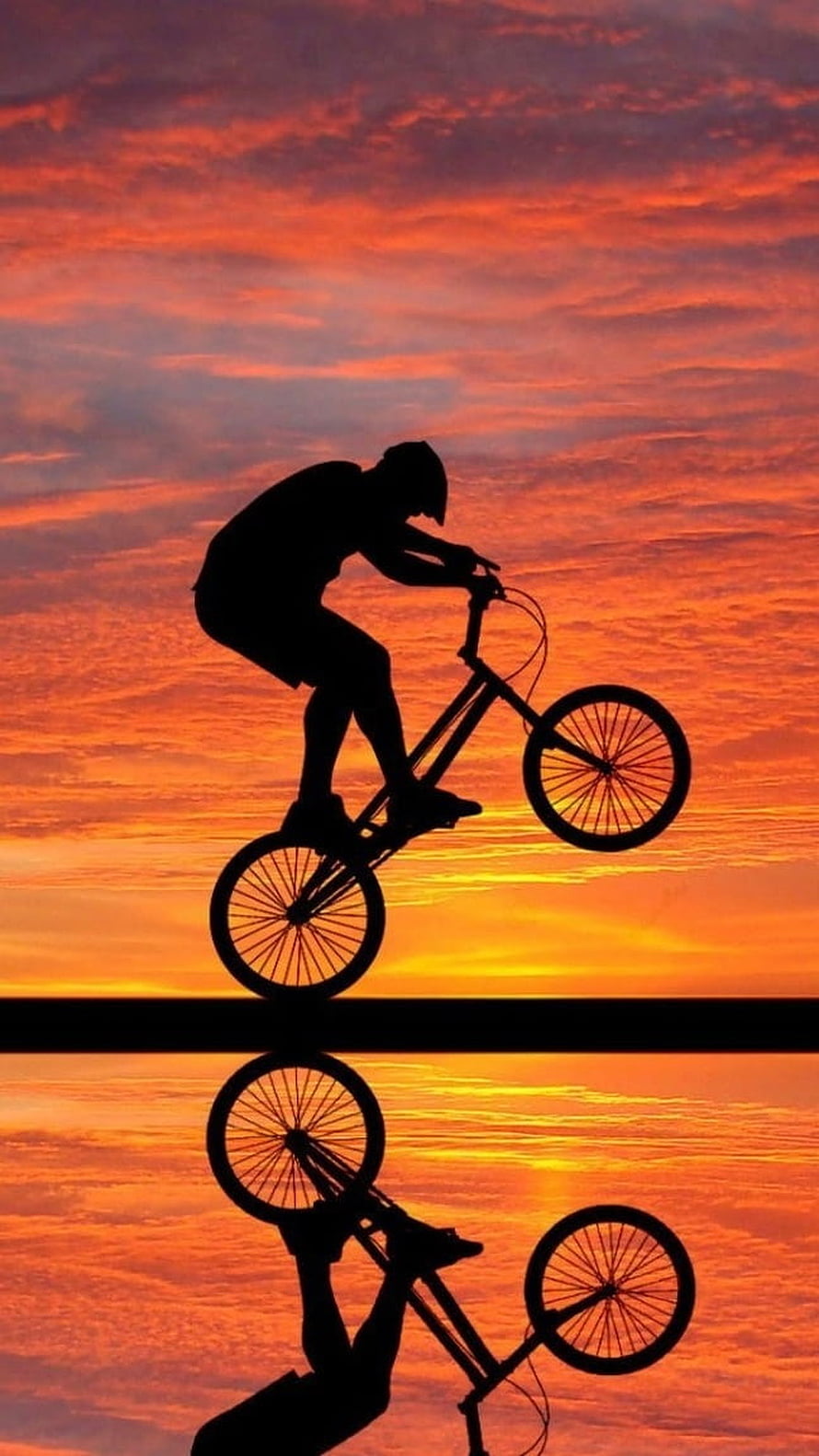 Silhouette of a BMX rider performing a jump against a fiery orange sunset sky HD phone wallpaper