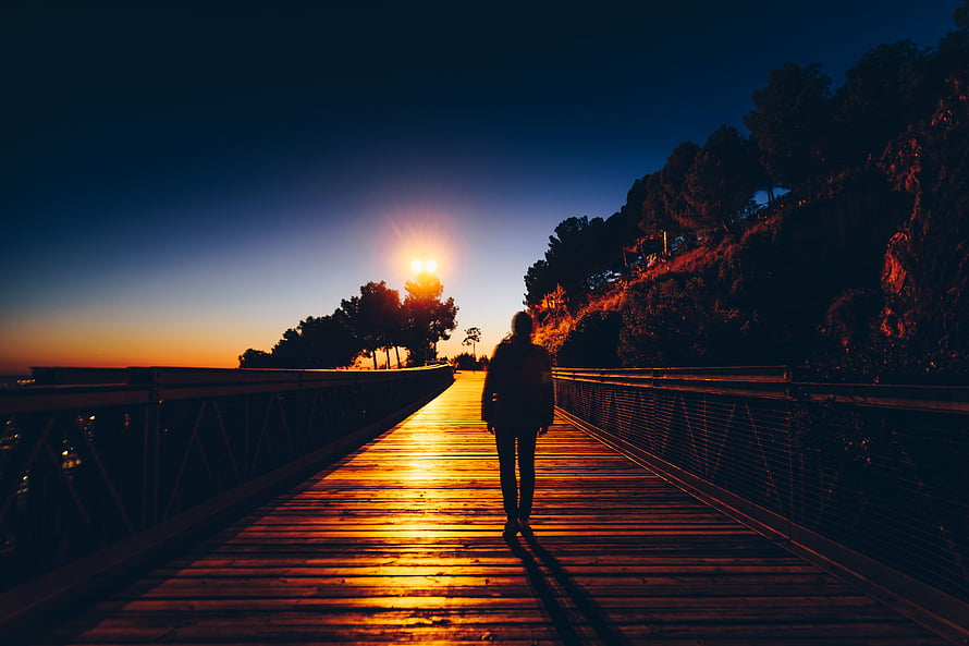 Silhouette of a person walking on a wooden pier at sunset with warm golden light HD wallpaper