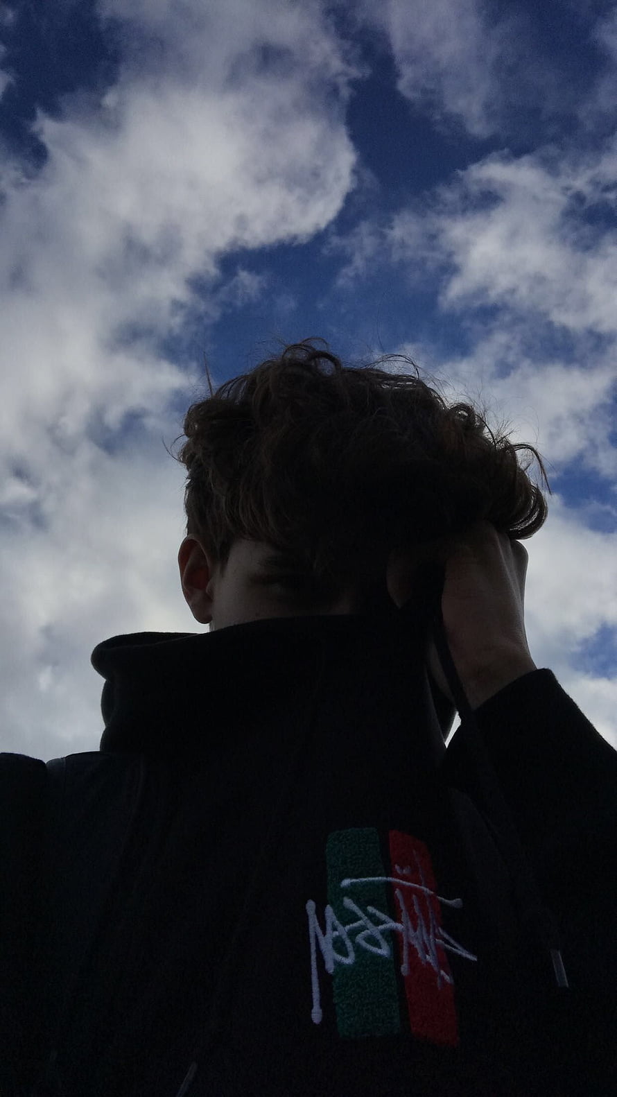 Moody Low-Angle Portrait of a Young Man in a Black Hoodie Against a Cloudy Blue Sky HD phone wallpaper