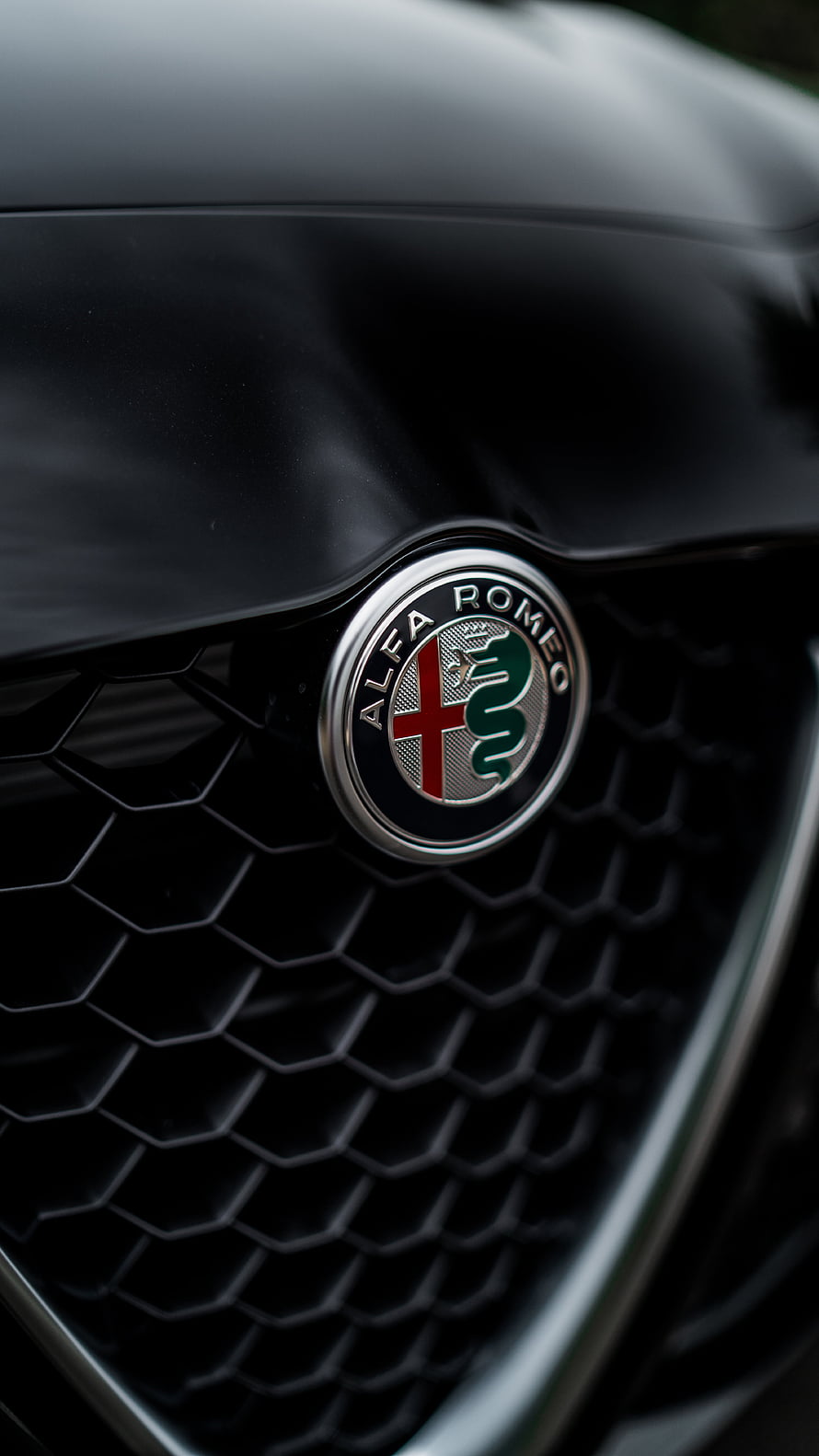Close-up of the Alfa Romeo badge on a black honeycomb car grille HD phone wallpaper