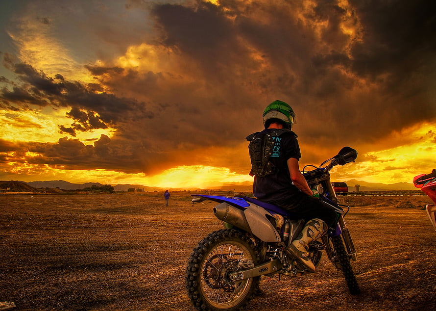 Motorcyclist on a dirt bike silhouetted against a dramatic golden sunset sky HD wallpaper