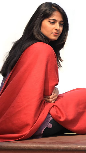 Anushka Shetty in a flowing red sari with long dark hair against a bright white background HD phone wallpaper